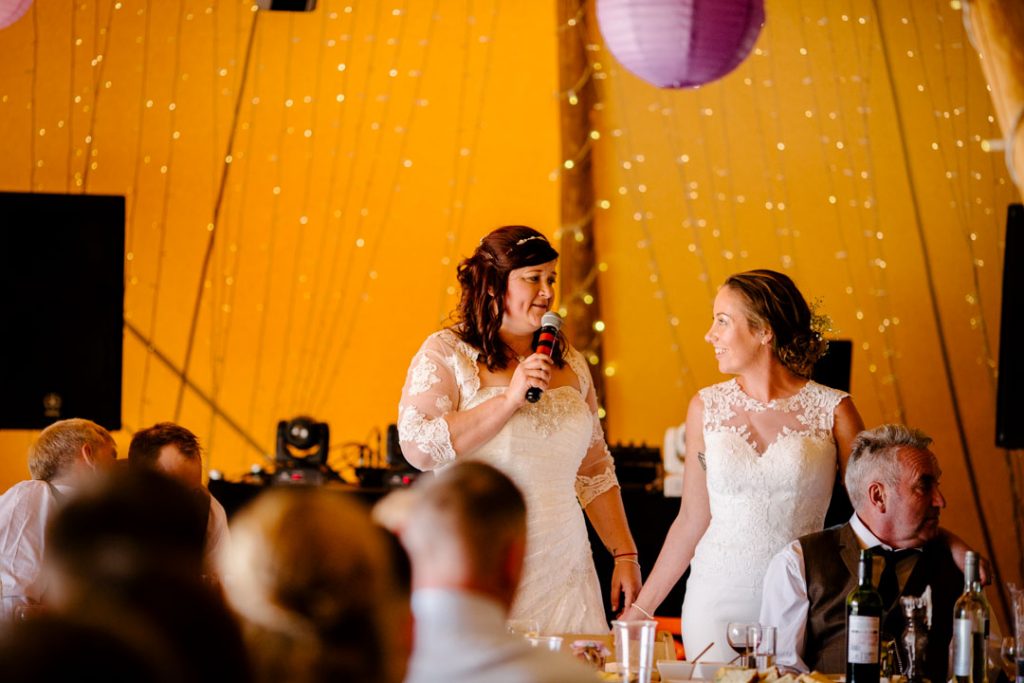 Two brides giving a speech at wedding breakfast. tipi wedding in stratford 