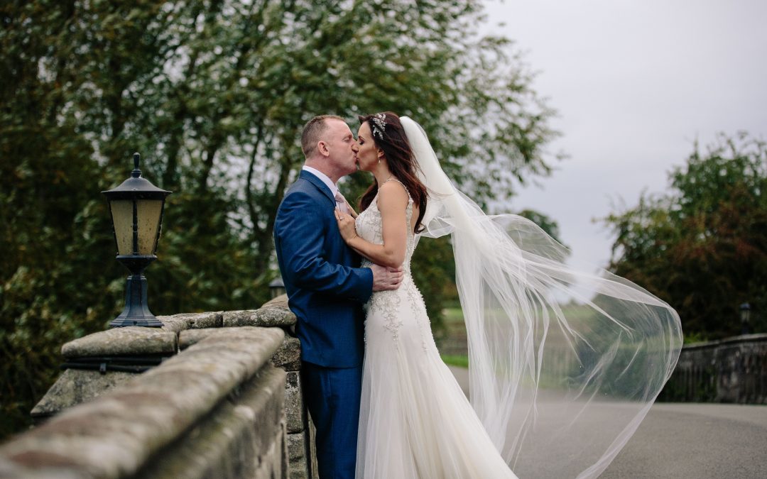Bride & groom kissing on the bridge at Walton hall. Bride's veil is blowing in the wind