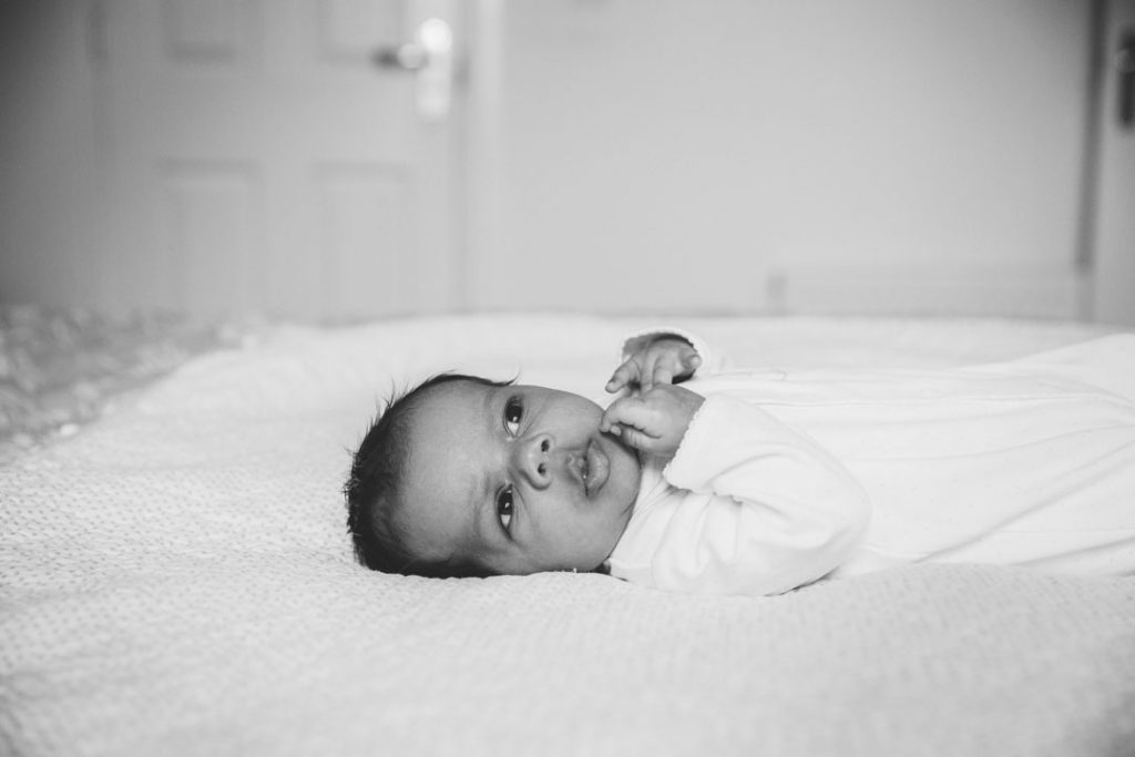 black & white image of newborn baby boy, lying on Mum's bed