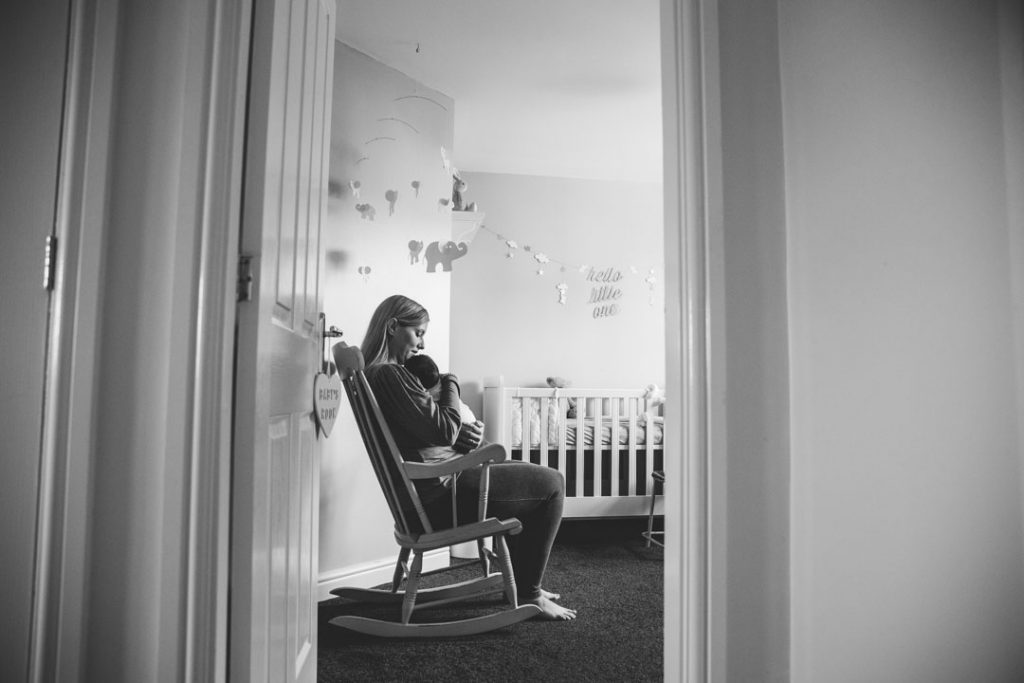 Black & white image of Mum holding baby in the nursery, sitting in a rocking chair. Solihull newborn photoshoot

