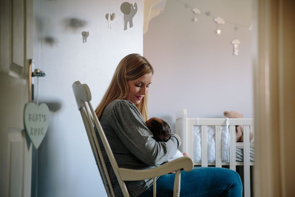 Mum holding baby boy, sitting in rocking chair in the nursery