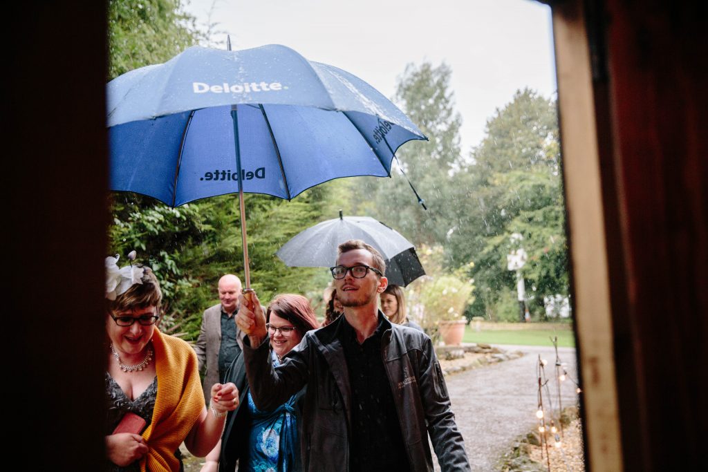 guests walking into wedding ceremony under umbrellas in the rain