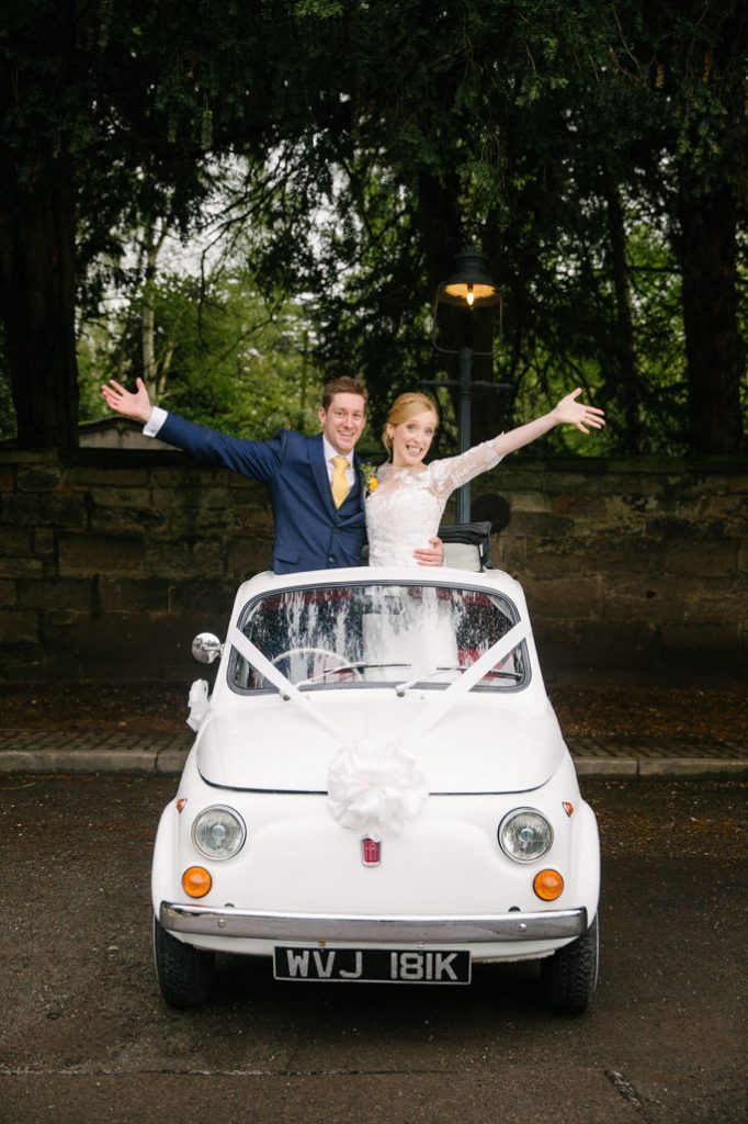 Bride and Groom standing up through roof of Fiat 500 wedding car, Saxon Mill