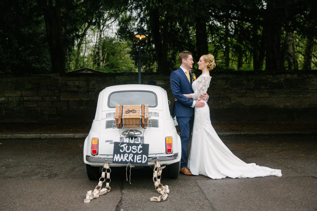 Bride and Groom standing leaning against Fiat 500 wedding car with just married sign, Saxon Mill