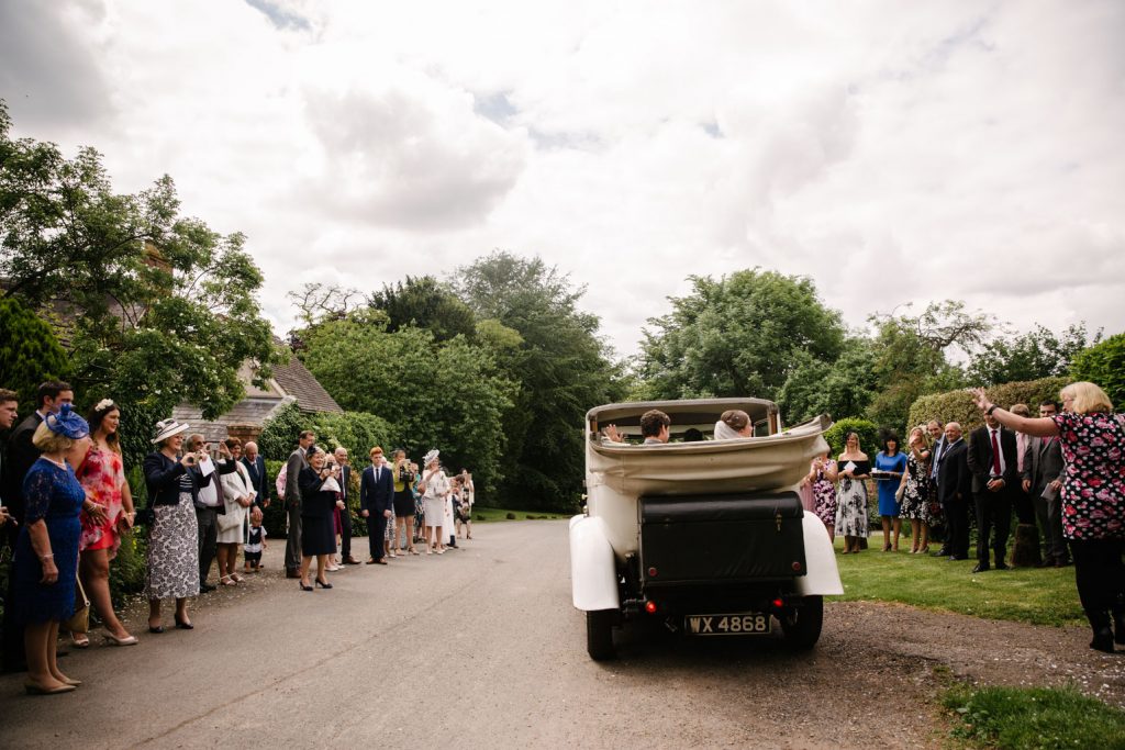 Bride and groom leaving church in their open top wedding car