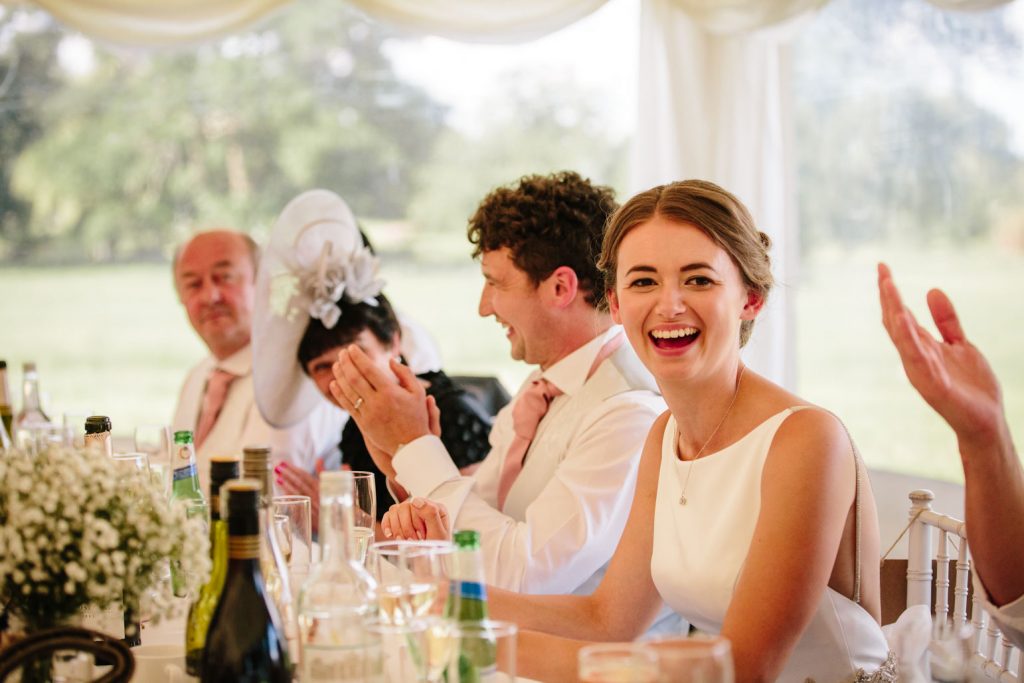 Bride laughing during wedding speech in marquee