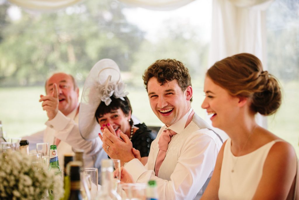 Groom laughing during wedding speech in marquee