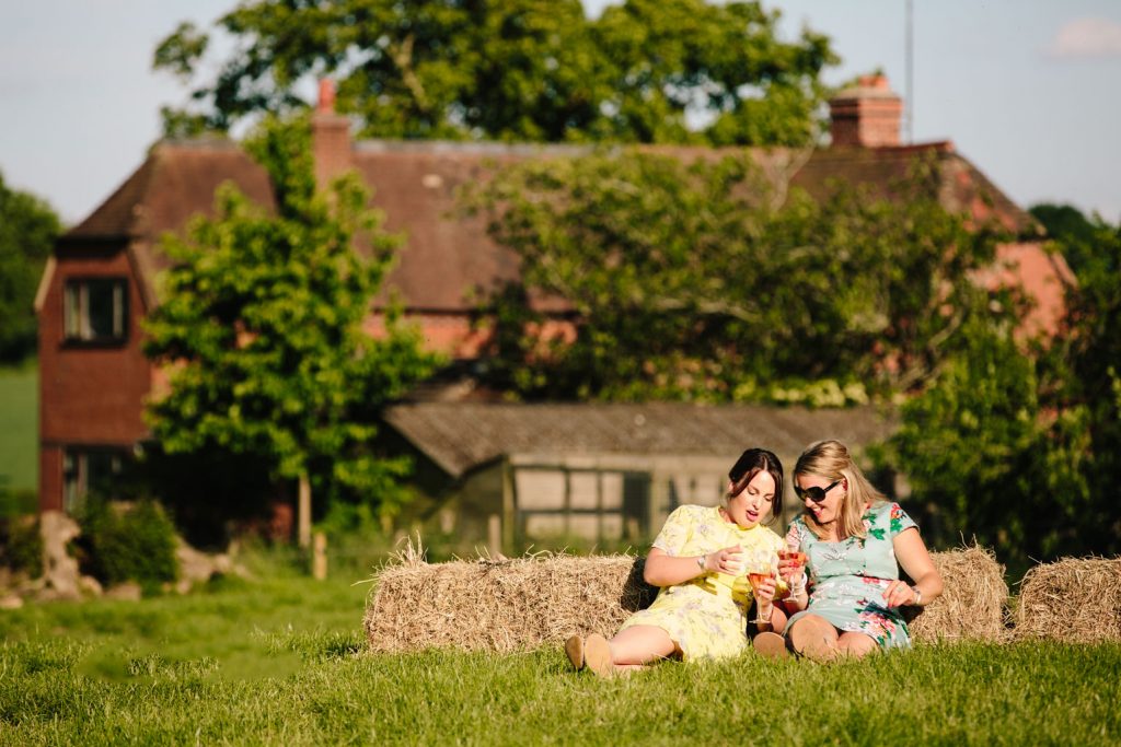 Two guests leaning against hay bales, drinking wine at a marquee wedding