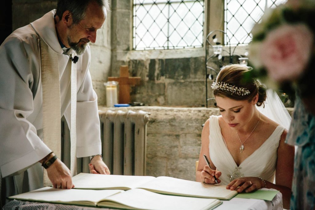 Bride signing the register in tan worth in Arden church wedding
