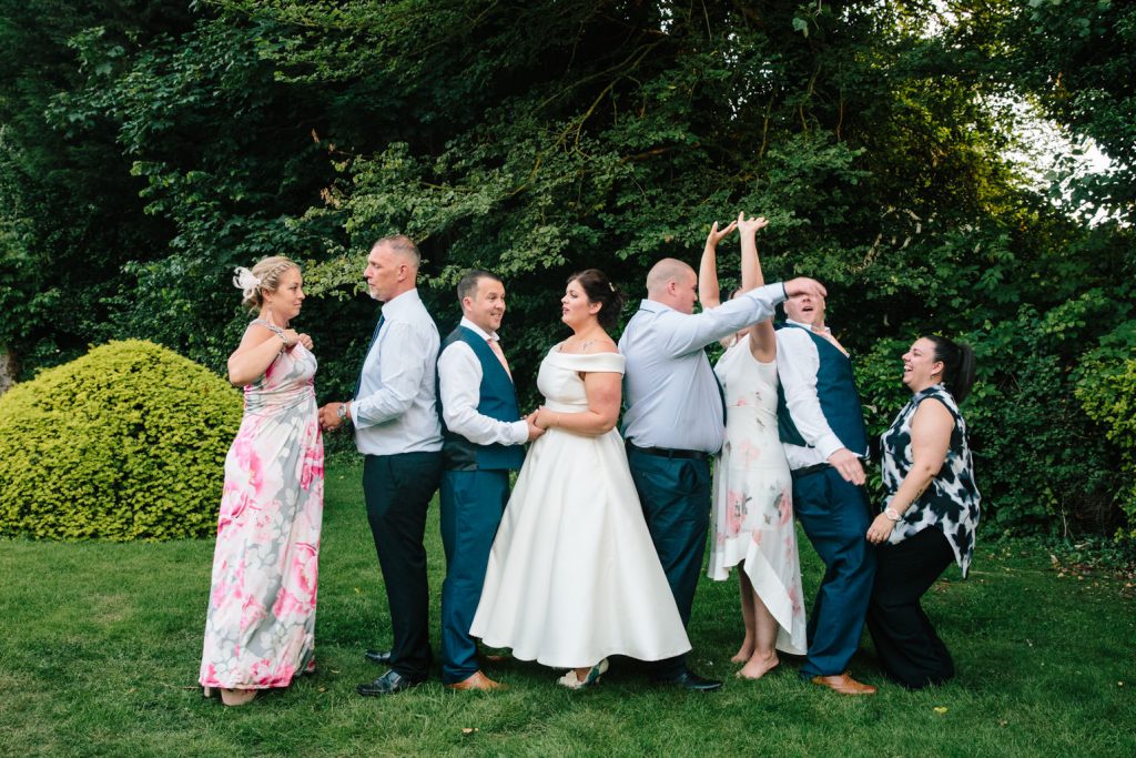 Bride and groom laughing with guests for a group photograph, manor by the lake wedding