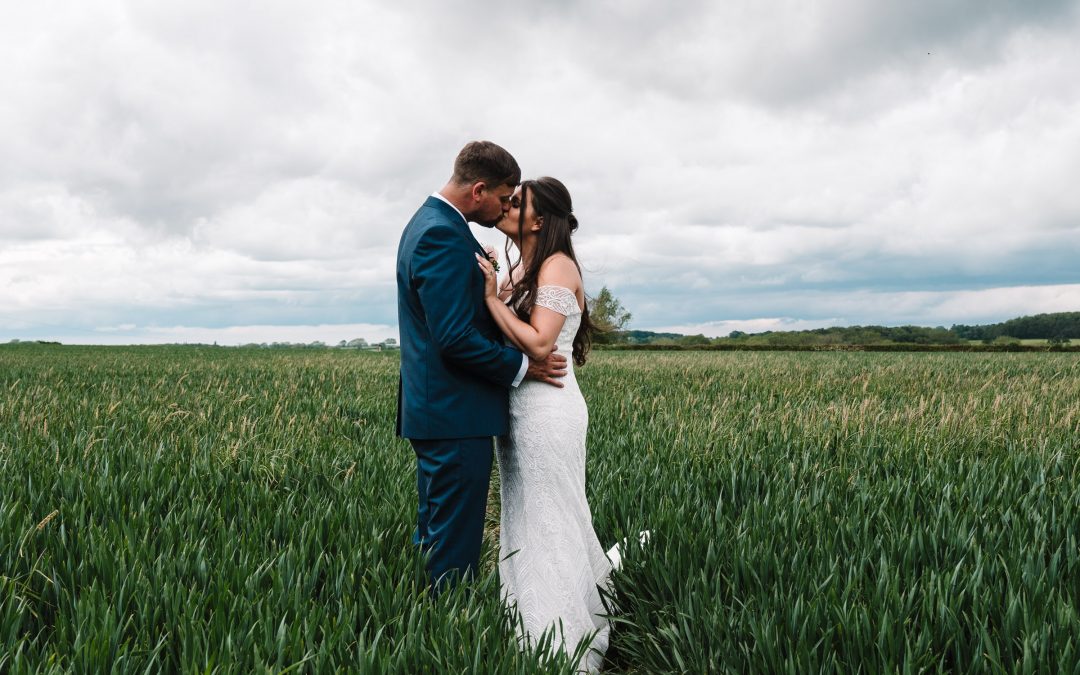bride and groom standing in a field kissing