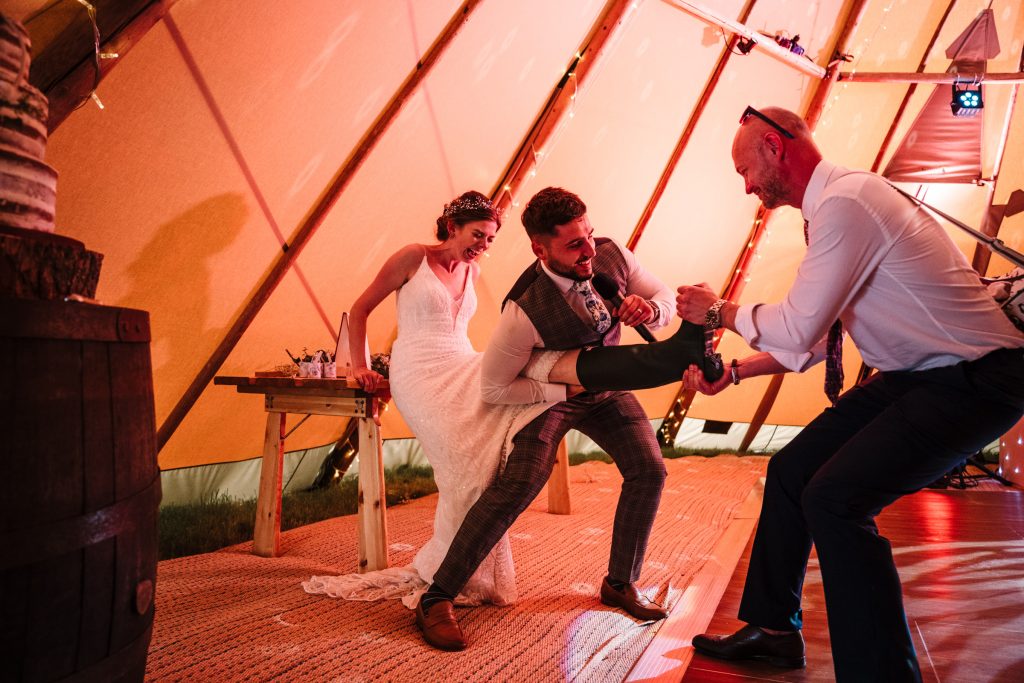 Groom and friend trying to pull welly off bride