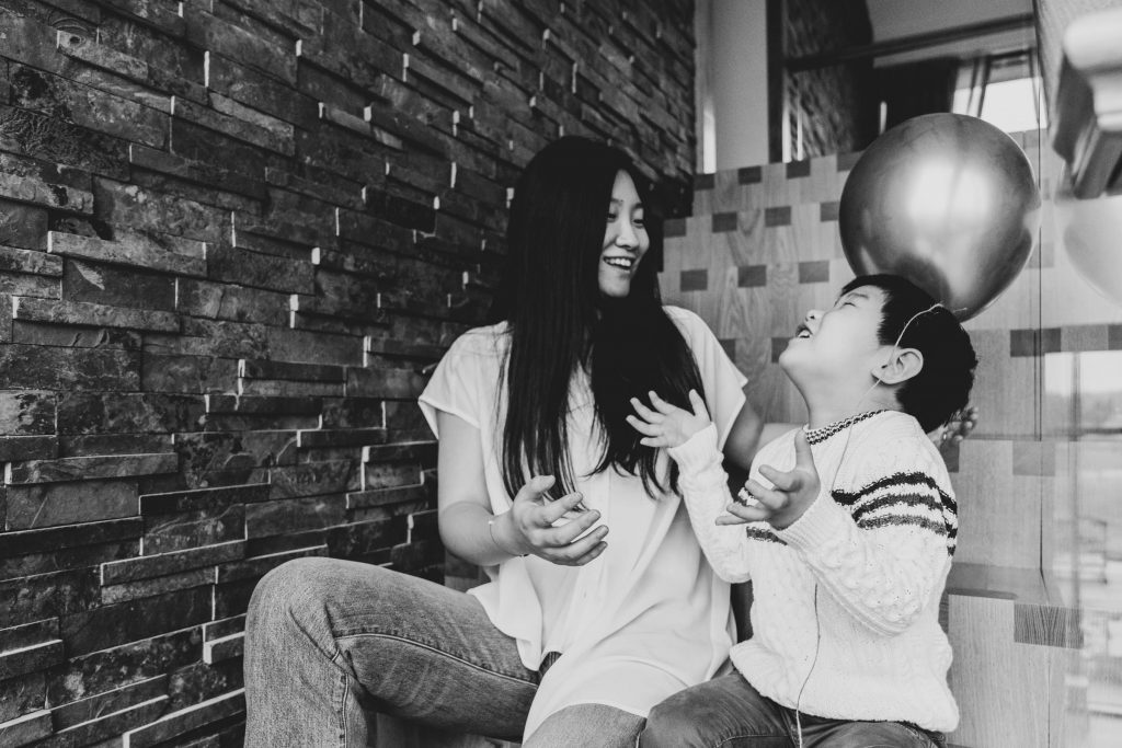 Mum and son laughing together on the stairs, playing with a balloon during family photoshoot at home 

