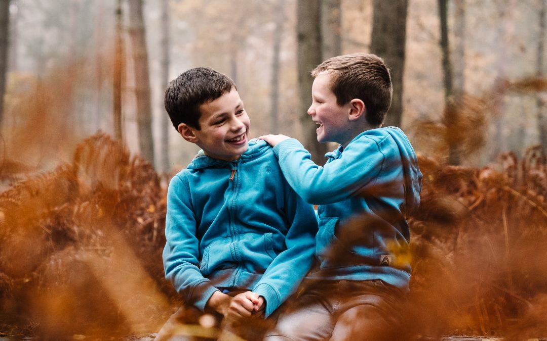 2 brothers sitting on a log in the woods, laughing