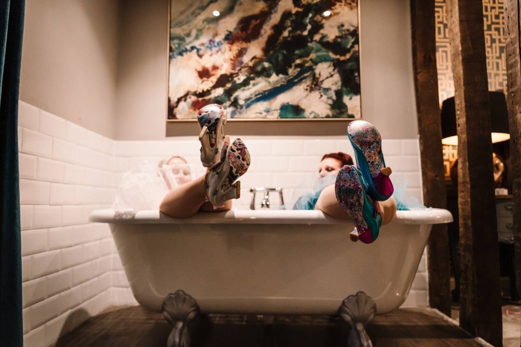 bride and bridesmaid sitting in the bath showing their irregular choice shoes