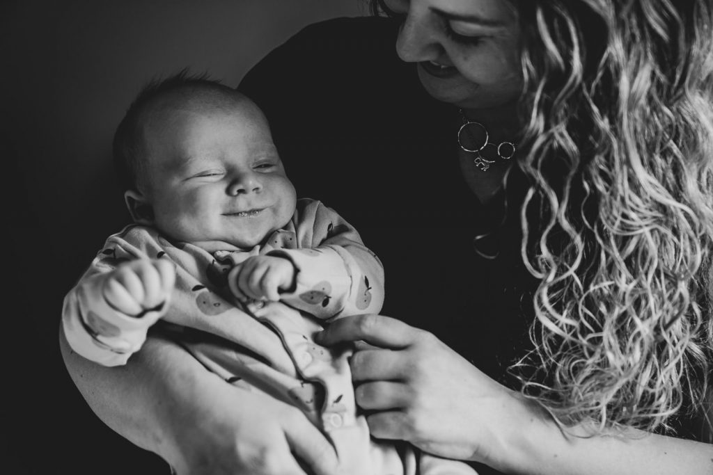 Baby smiling as he is cuddled by Mum during newborn photoshoot 