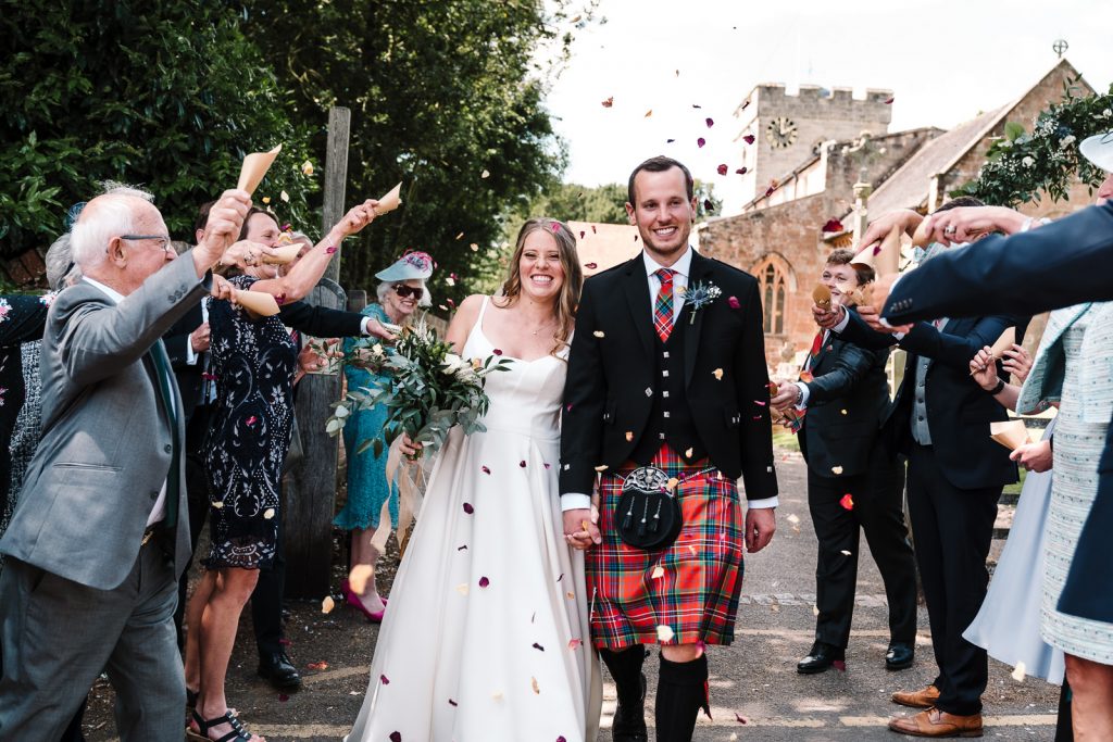 Bride and groom walking as confetti is thrown by wedding guests 
