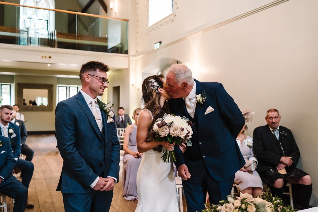 bride kissing dad as he gives her away at wedding ceremony