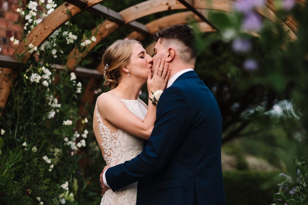 bride and groom kissing in flower arch