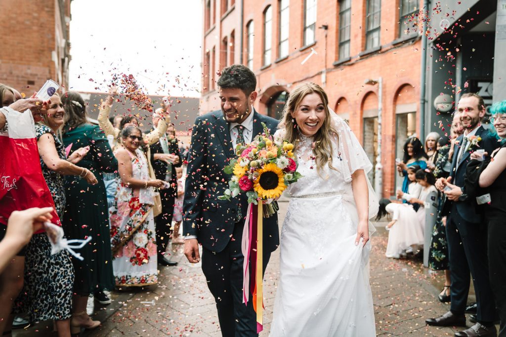 bride and groom walking through confetti cannons in the street at custard factory wedding 