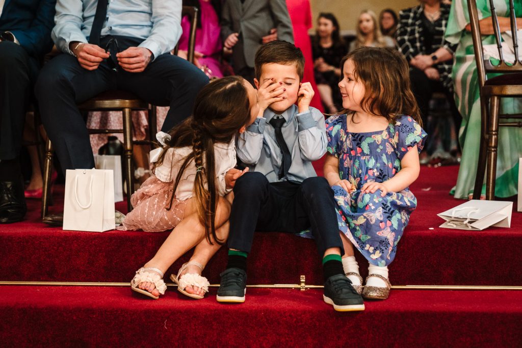 boy grimicing as girl kisses him at wedding