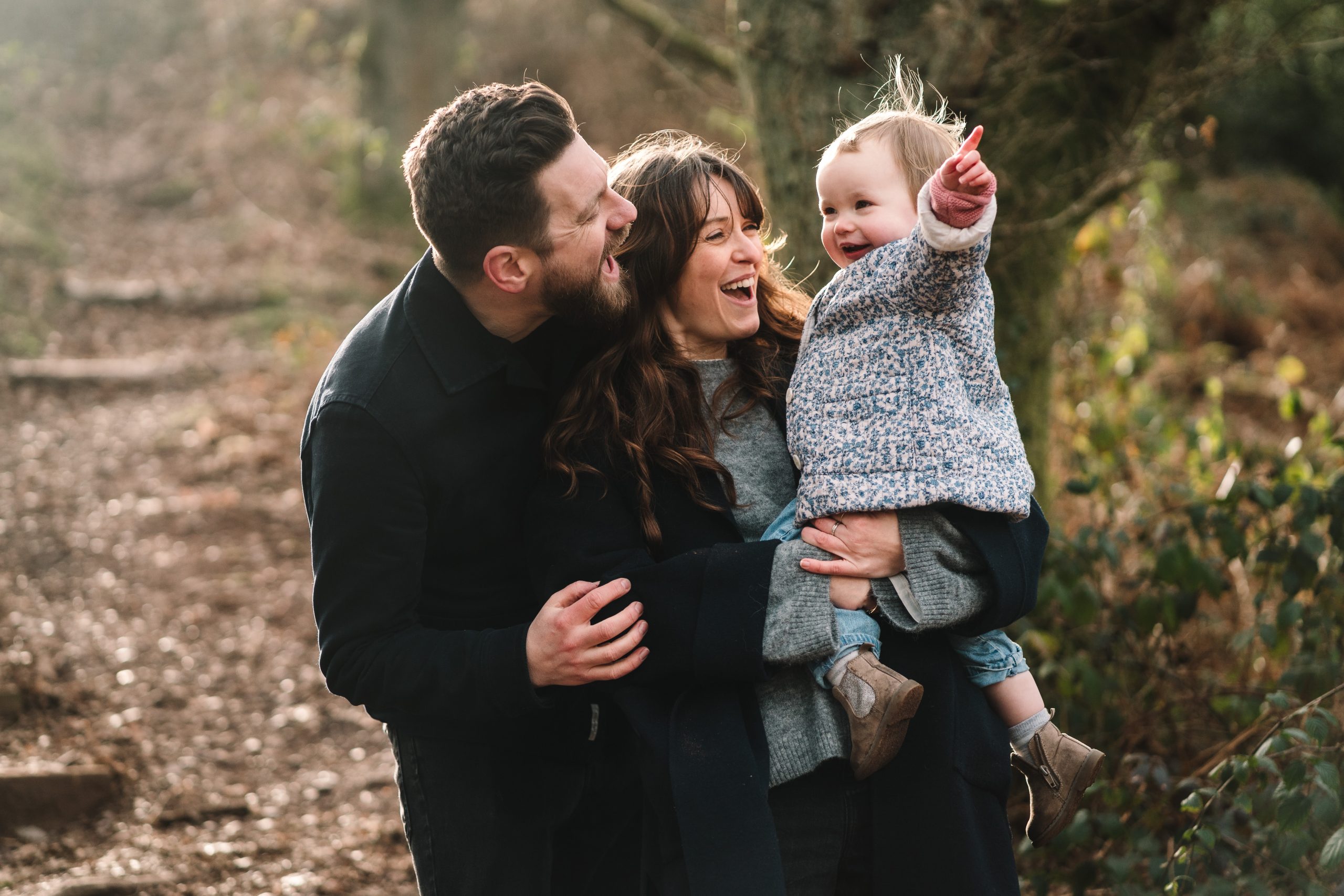 Mum and dad cuddling their 2 year old daughter out in the woods on a family shoot